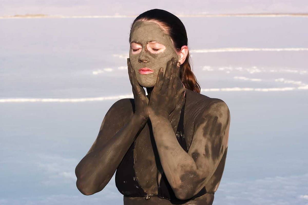 Young adult Israeli woman enjoying the natural mineral mud sourced from the dead sea, Israel. The Dead Sea known for its healthy minerals and as the lowest point on earth.(1,300 feet below sea level)