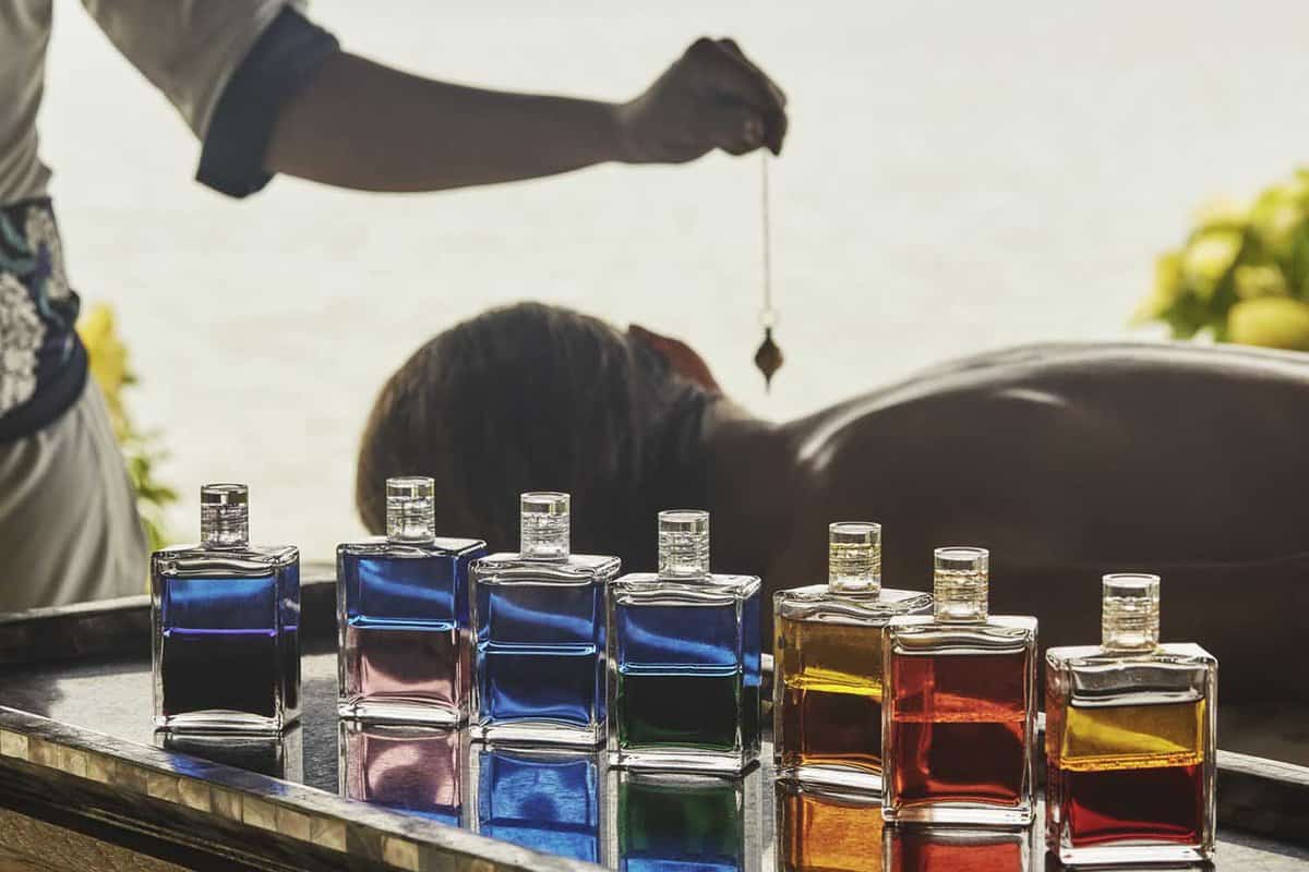 Bottles filled with colourful liquids and in background woman dangling an energy crystal over a guest