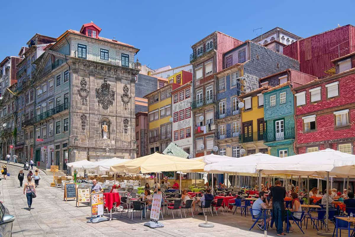 Colorful houses and outdoor cafes at historic Ribeira Square of Porto, a popular place for tourists and locals.