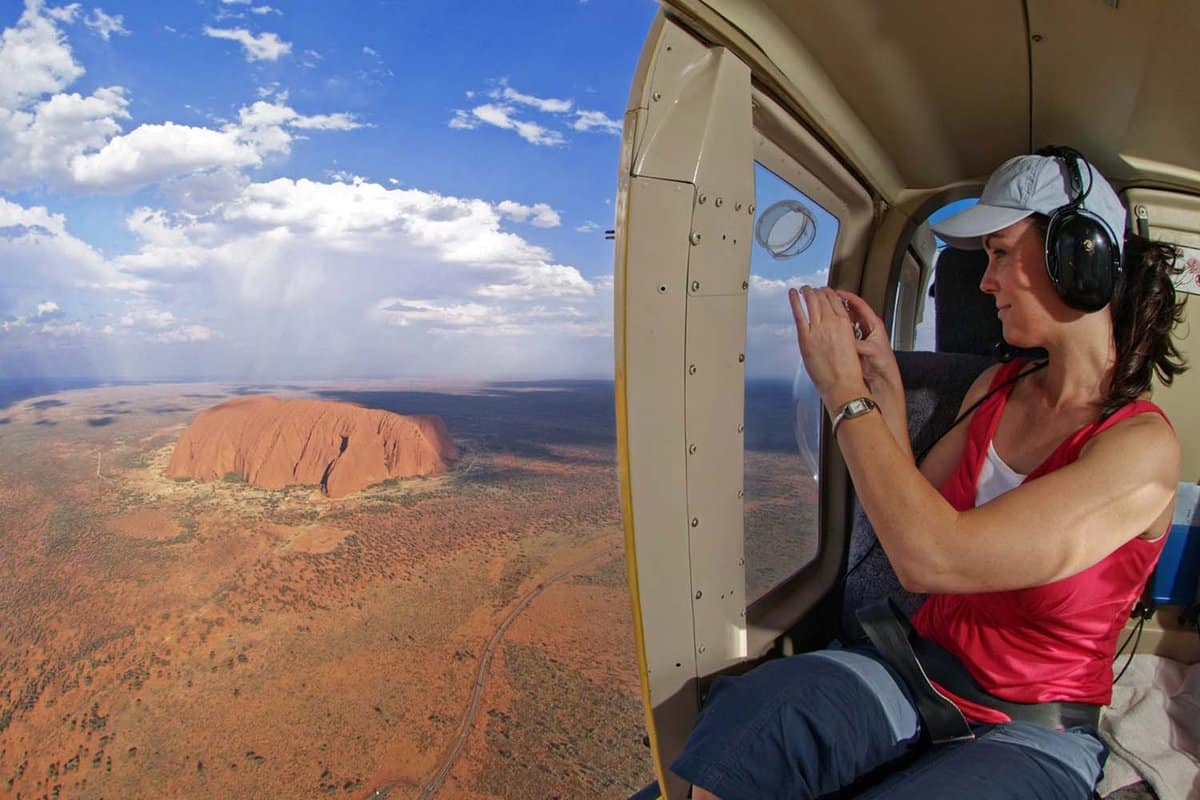 Woman taking a photo or Uluru in back of a helicopter