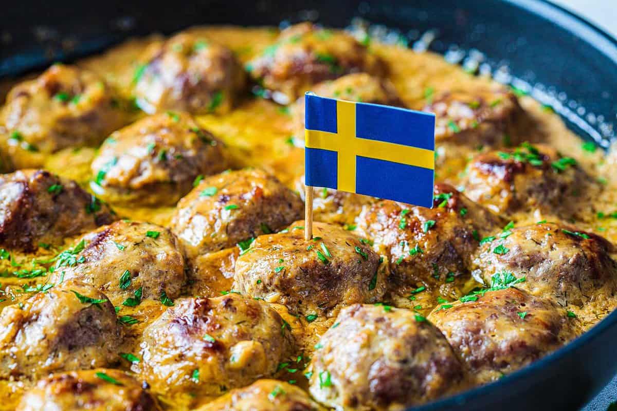 Swedish meatballs in a creamy sauce in a black frying pan, gray background, close-up. Scandinavian food concept.